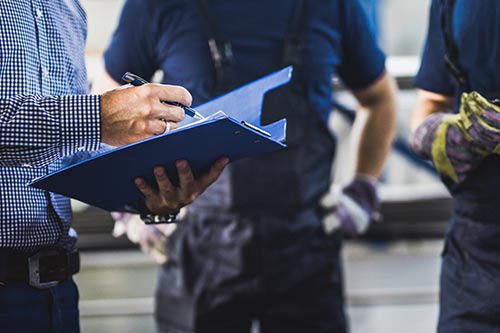 A warehouse manager helps to solve a supply and logistics challenge as he reviews data on his clipboard.